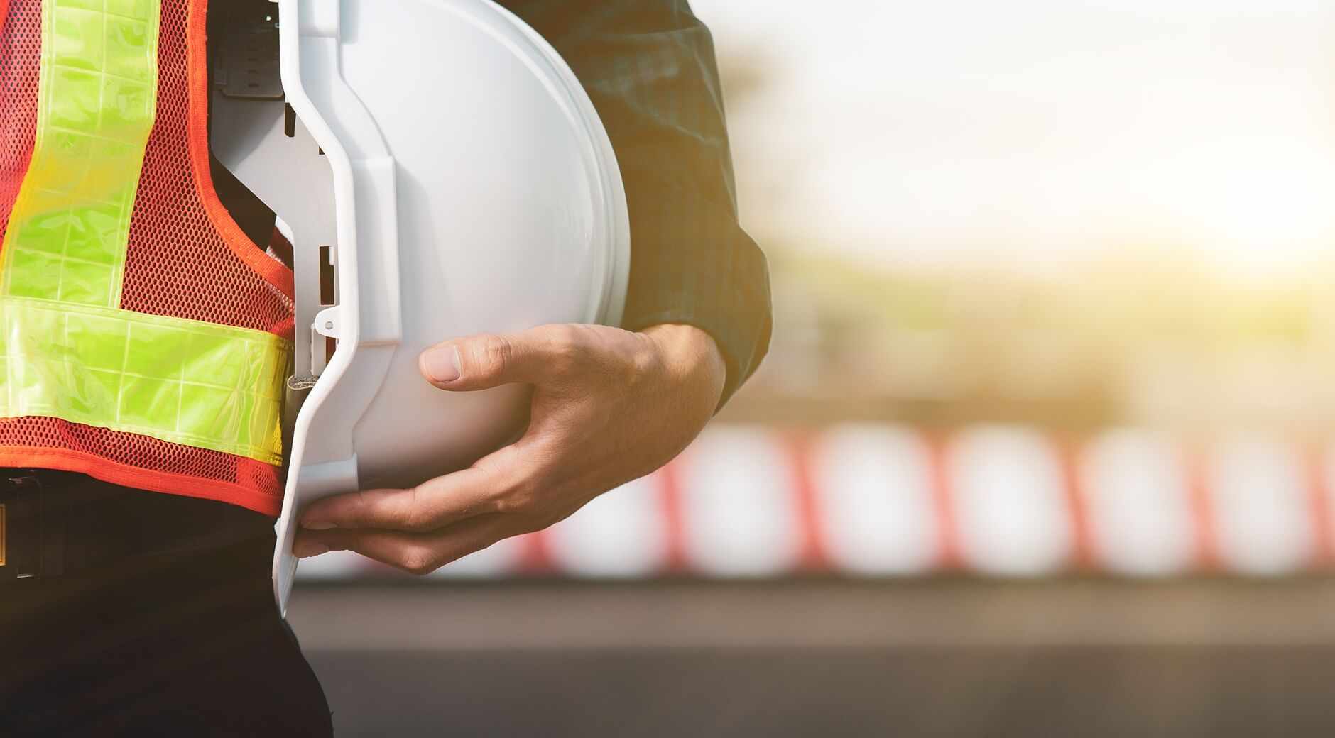 Construction worker holding a white hard hat while wearing a safety vest.